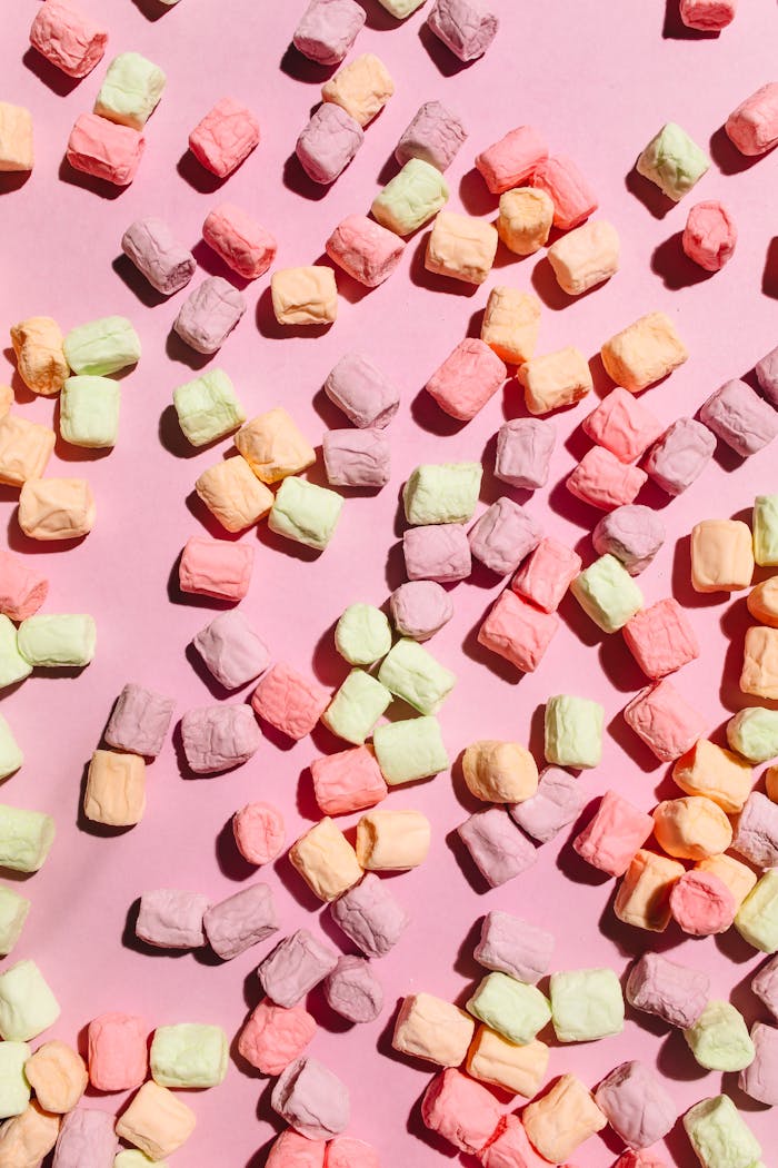 Pastel marshmallows scattered on a pink surface creating a soft, playful scene.