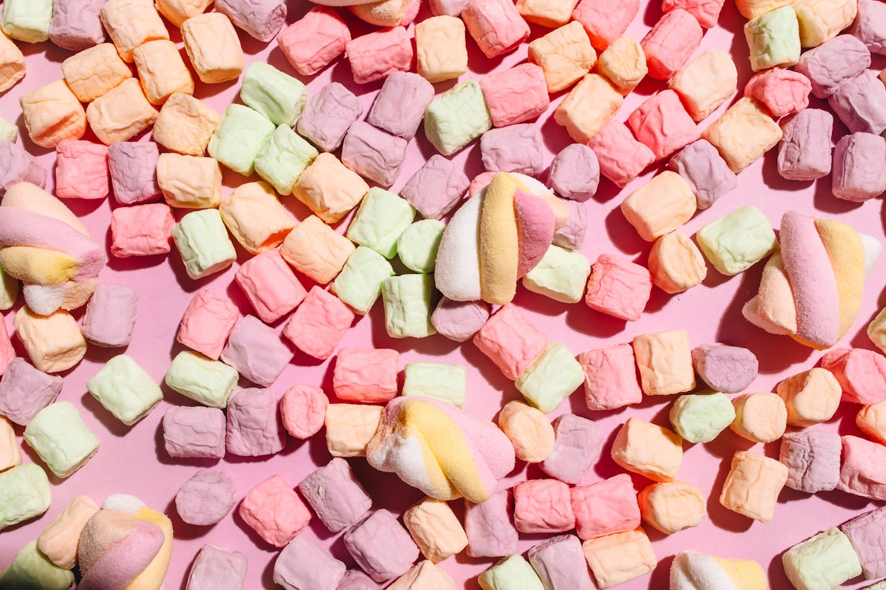 Vibrant pastel marshmallows scattered on a pink surface, creating a soft, playful appearance.